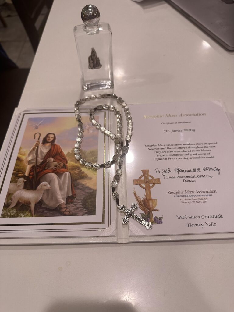 Rosary beads and holy water gifted to Dr. James Wittig from Lourdes, with a prayer card and certificate of enrollment.