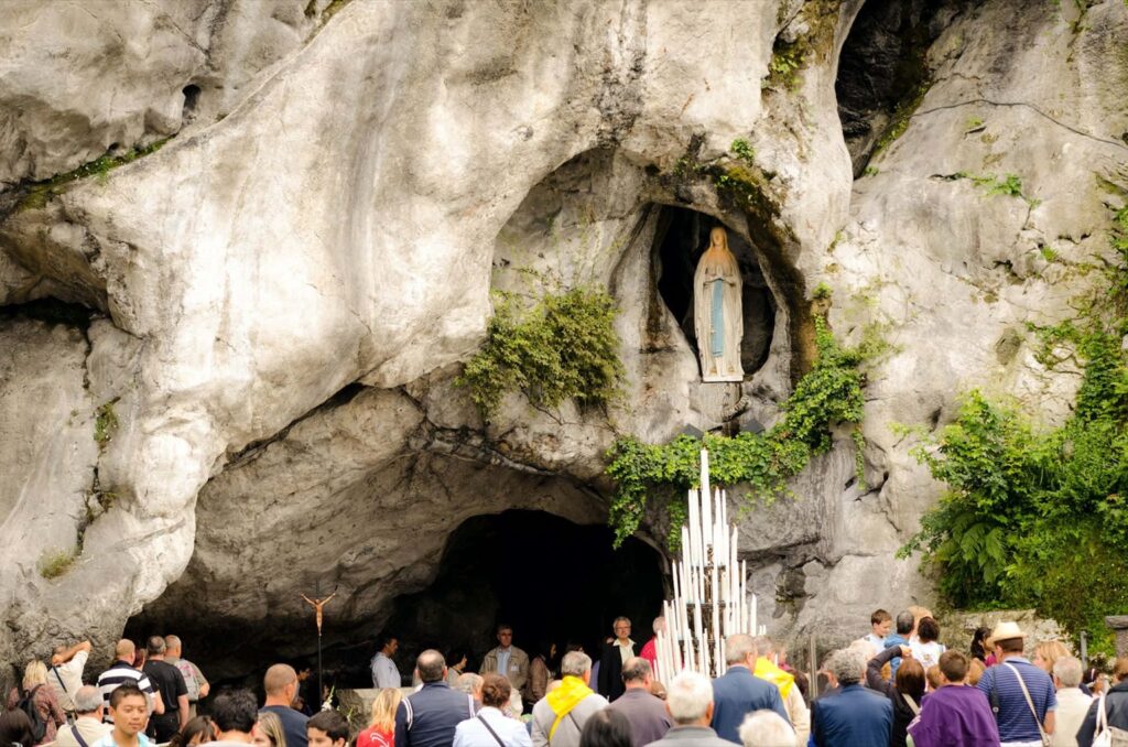 Pilgrims gather at the Grotto of Our Lady of Lourdes in France, beneath the statue of the Virgin Mary.
